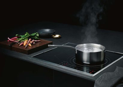 Modernes Induktionskochfeld mit kochendem Topf und frischem Gemüse. Hochwertige Küchentechnik von AEG