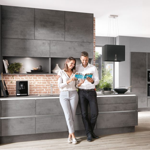 Paar steht in moderner Designküche und schaut gemeinsam in ein Kochbuch.