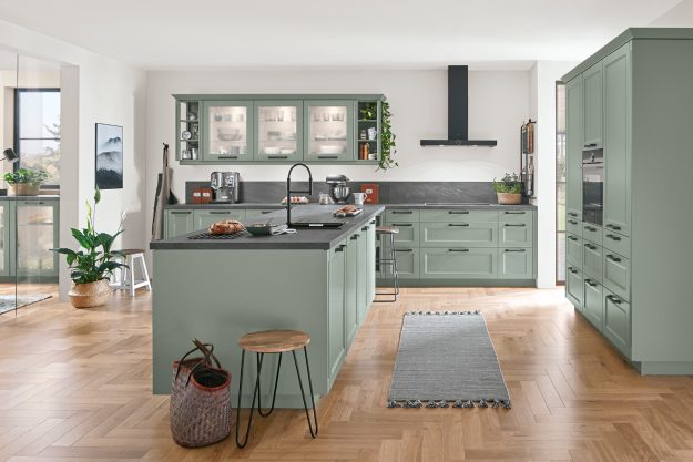 Moderne Landhausküche in sanftem Grün mit schwarzer Arbeitsplatte und Holzfußboden. Stilvolle Kombination aus Tradition und Moderne.