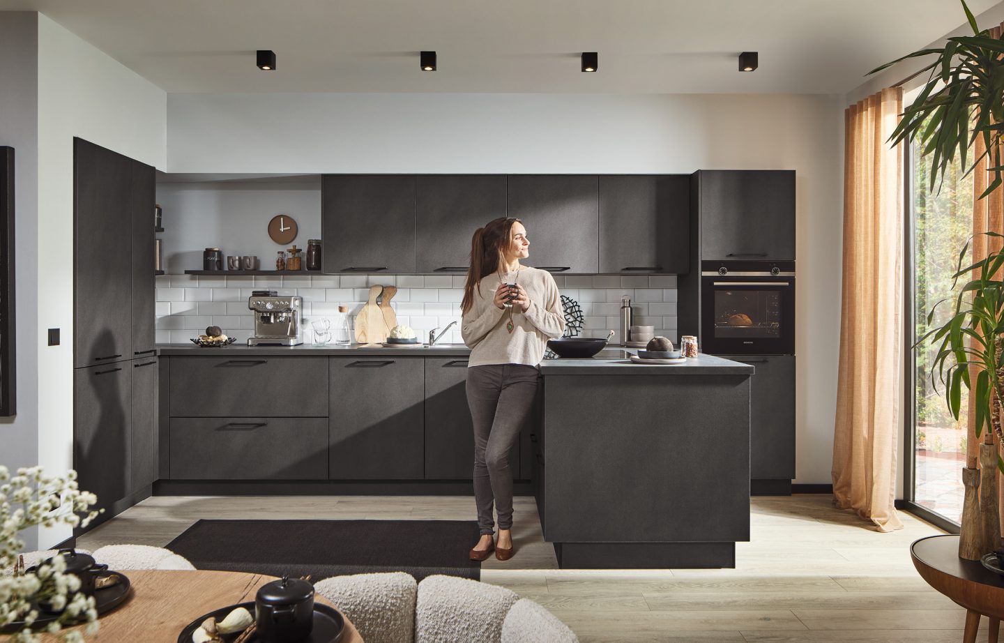 Frau in dunkler Küche lehnt an Kücheninsel mit Kaffeetasse